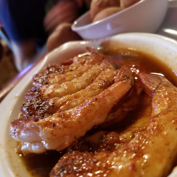 Plate of seasoned shrimp in a rich sauce, with a bowl of small potatoes in the background.