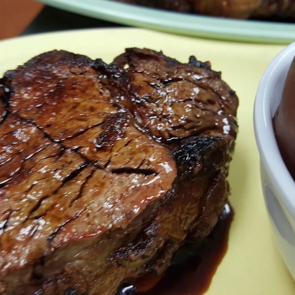 Grilled steak with a dark glaze on a yellow plate, next to a bowl of red potatoes.