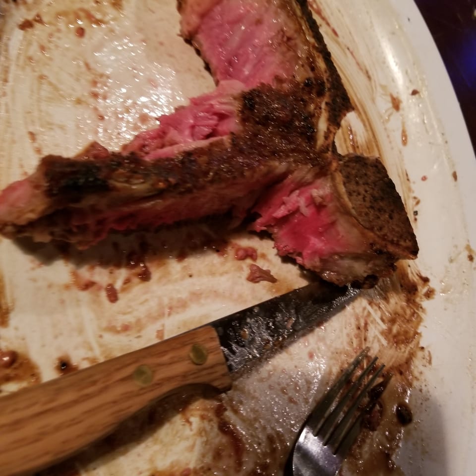 A partially eaten steak, medium-rare, on a white plate with a knife and fork.
