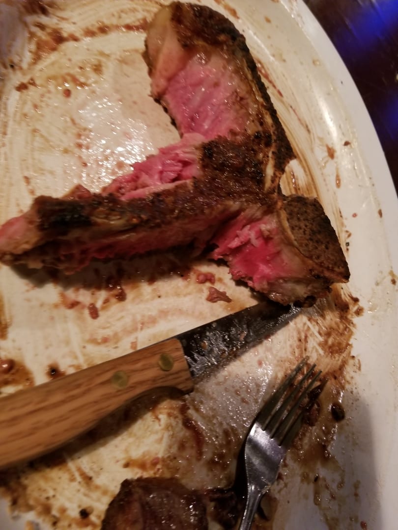 A partially eaten steak, medium-rare, on a white plate with a knife and fork.