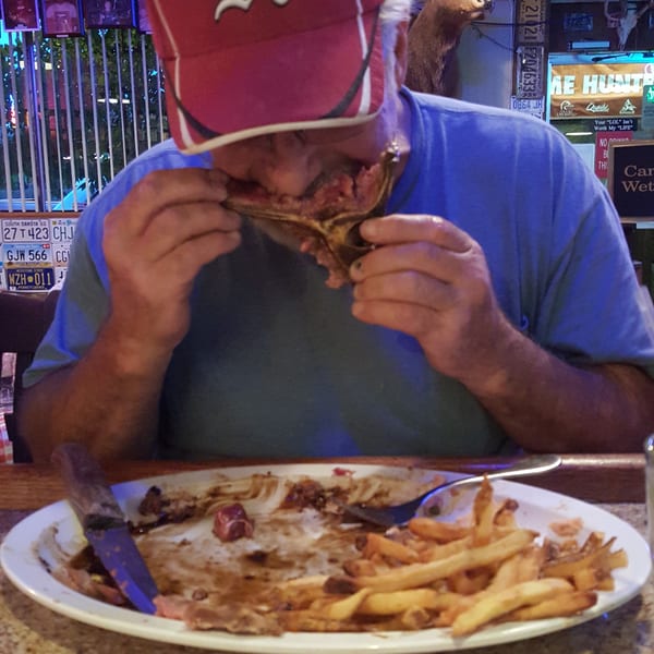 Man in a red baseball cap eating ribs and fries at a casual restaurant with a deer head mount.