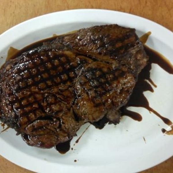 Grilled steak with prominent grill marks and a rich dark sauce on a white oval plate.