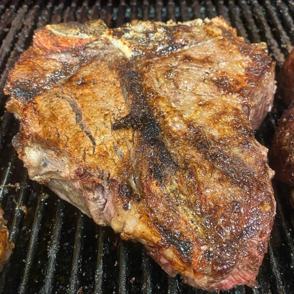 Large, juicy T-bone steak cooking on a hot grill with visible char marks.