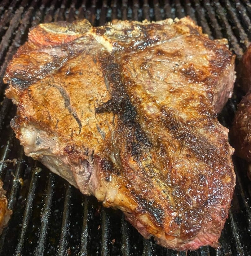 Large, juicy T-bone steak cooking on a hot grill with visible char marks.