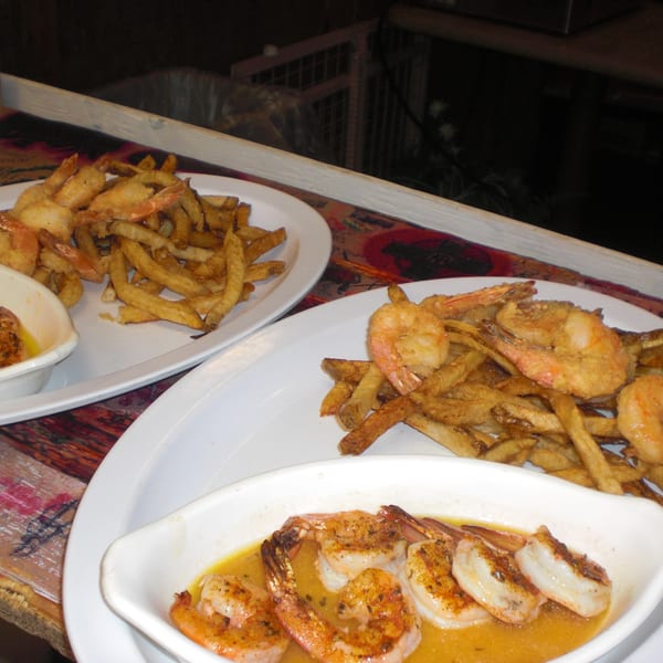 Two plates of fried shrimp and french fries, with a small dish of shrimp in sauce.