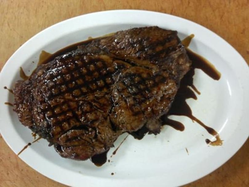 Grilled steak with grill marks and dark sauce on a white oval plate.