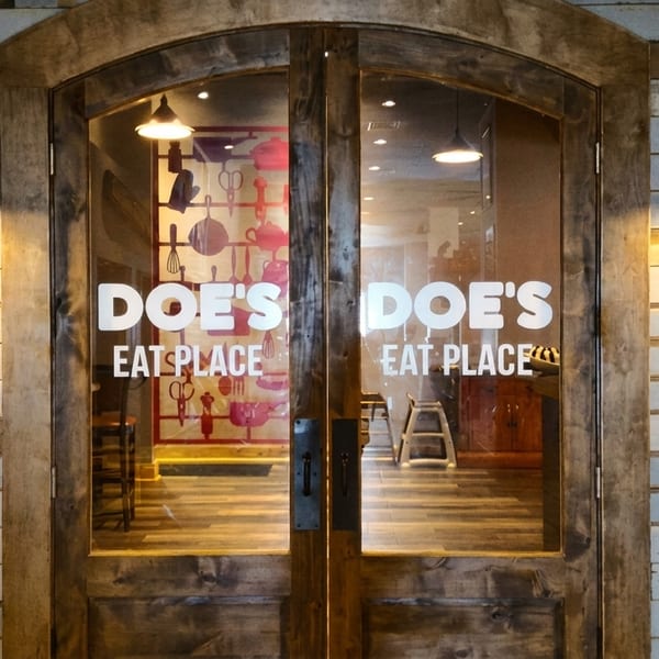 The entrance to Doe's Eat Place, featuring wooden doors, a rustic brick wall, and menu boards.