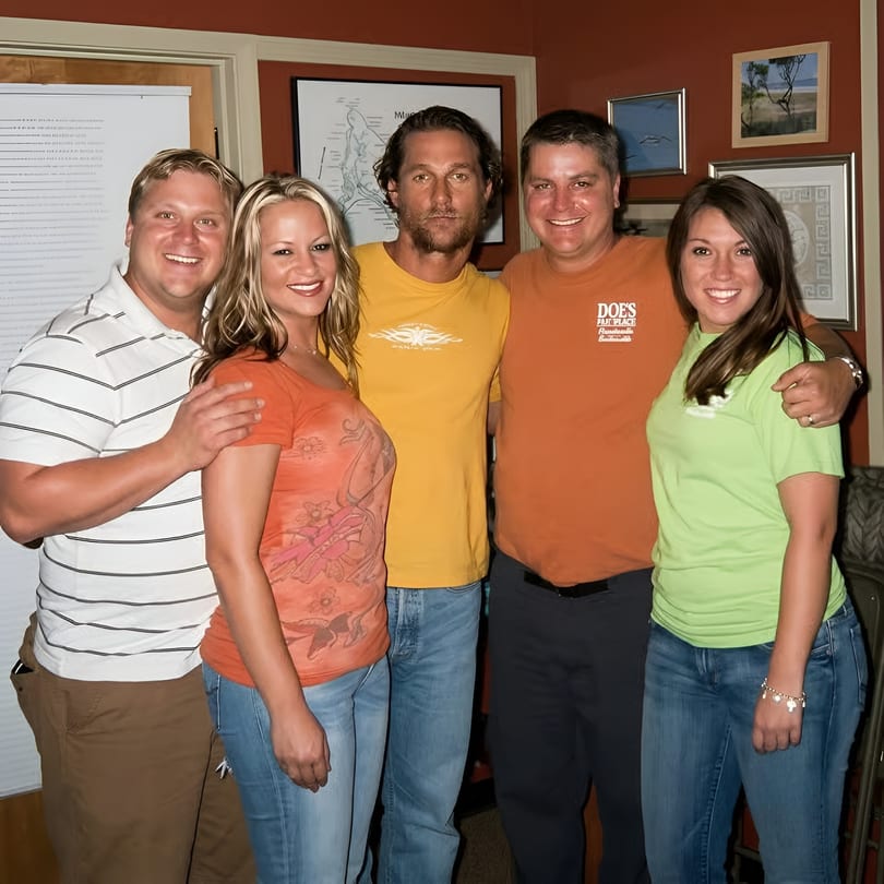 Five smiling people, including Matthew McConaughey, pose together in a restaurant with framed art.