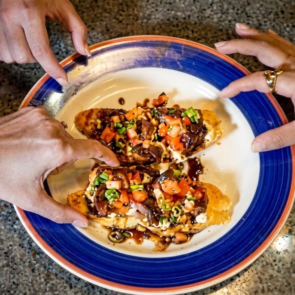 Four hands reaching for two bruschetta pieces topped with meat, tomatoes, and green onions.