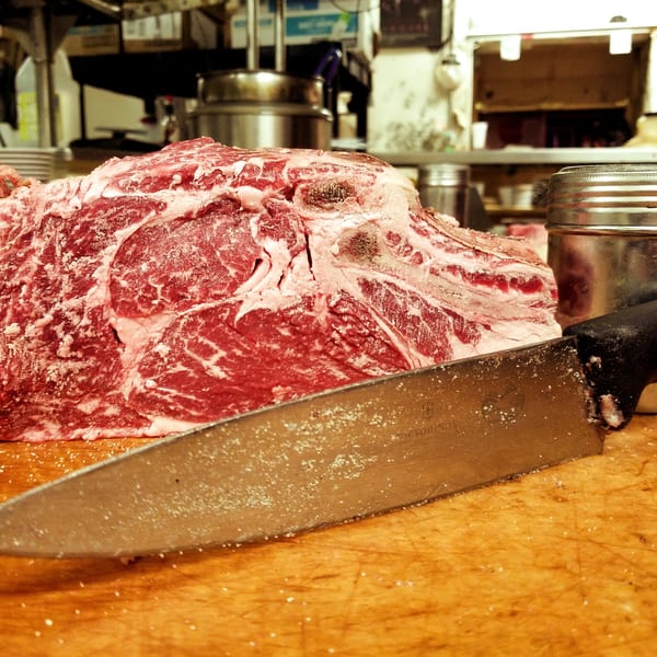 Raw, seasoned beef roast on a wooden cutting board with a large knife in a restaurant kitchen.
