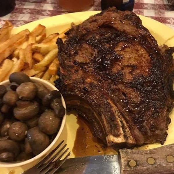 A juicy grilled steak, golden fries, and sautéed mushrooms served on a yellow plate.