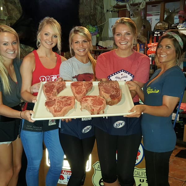 Five Doe's Eat Place staff members proudly display a tray of large raw steaks.