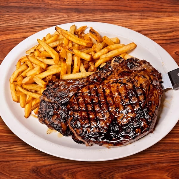Grilled steak and golden french fries on a white plate with a knife, set on a wooden table.