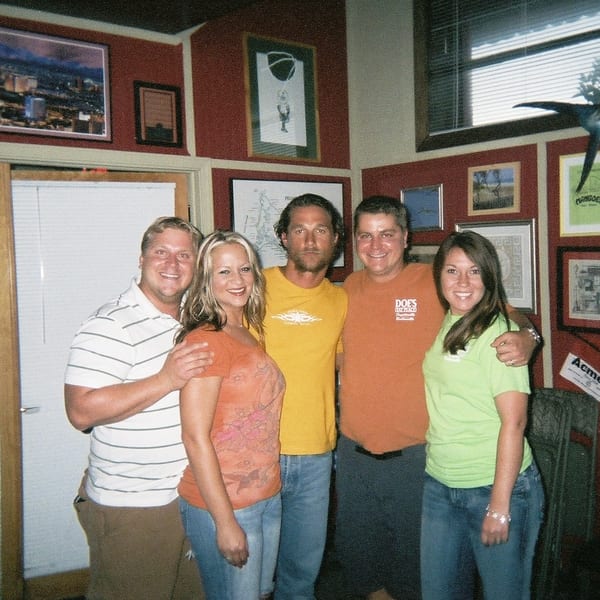 Five smiling people posing in a casual restaurant with red walls and framed art.
