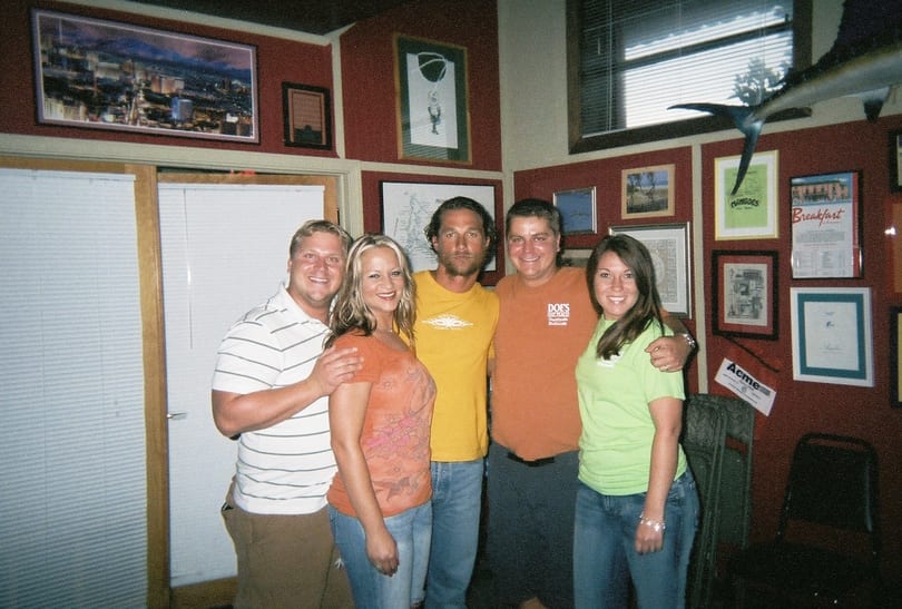 Five smiling people posing in a casual restaurant with red walls and framed art.