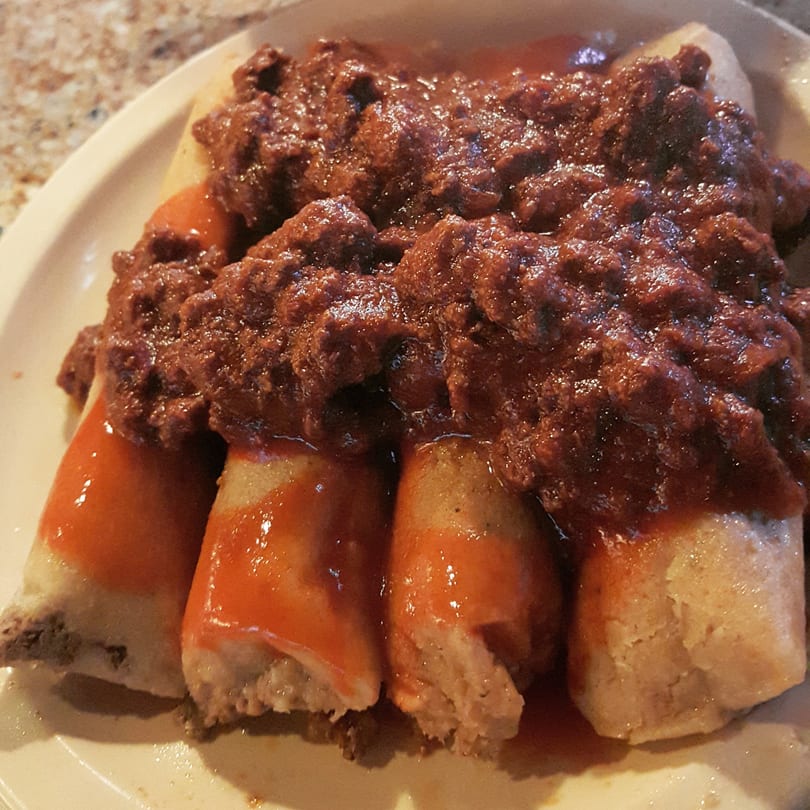 Close-up of several tamales smothered in a savory dark red chili sauce.